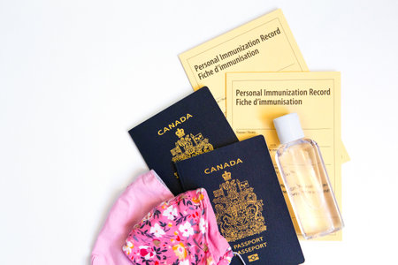 Two Canadian passports with yellow immunity vaccination records, face cotton protective masks and sanitizer. Safety measuresの写真素材