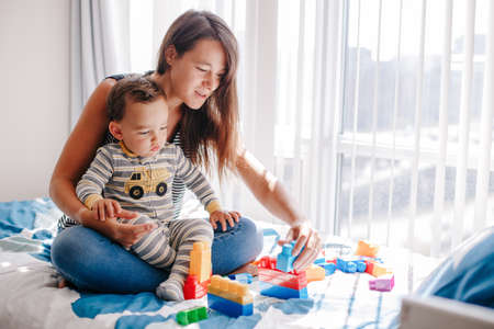 Mother and baby toddler playing building with learning toy stacking blocks at home. Early age...