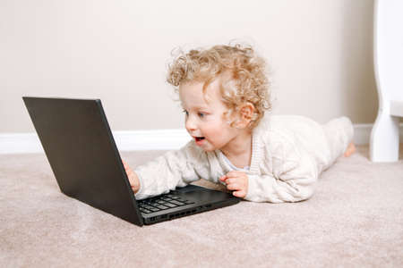 Cute blonde curly toddler baby boy working on laptop. Little kid child using technology. Early age education development. Video chat, video call. Computer screen time for children.の写真素材