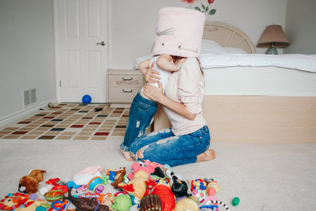 Mother parent playing with baby toddler in bedroom. Mom and kid boy girl with toy bin on heads. Family having fun at home. Candid authentic happy childhood lifestyle. Family life with kids.の写真素材