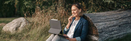 Woman working on laptop in park o . Student studying learning online. Video blogger doing live stream. Web banner header.の写真素材