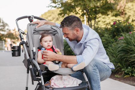 Caucasian proud father walking with baby daughter in stroller. Family dad and daughter together outdoor in city street on summer day. Urban life with kids children. Happy lifestyle family.の写真素材
