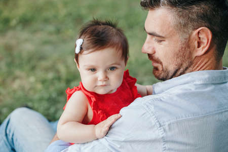 Middle age Caucasian proud father holding baby daughter. Family dad and daughter sitting together outdoor in park on summer day. Life with kids children. Happy lifestyle family of two.の写真素材