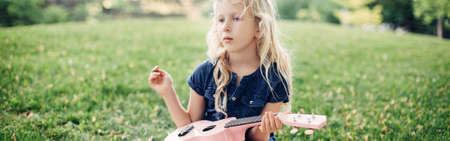 Girl playing pink guitar toy outdoors. Child playing music and singing song in park. Music hobby activity for children kids.Real authentic candid childhood moment. Web banner header.の写真素材