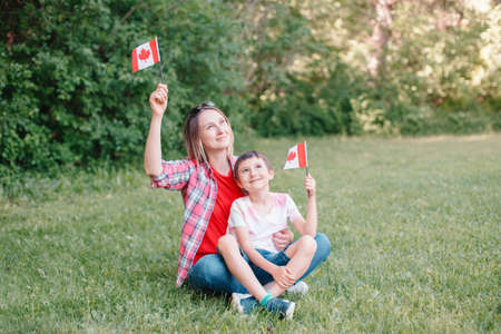 Family mom with son celebrating national Canada Day on 1st of July. Caucasian mother with child boy waving Canadian flags. Proud citizens celebrate Canada Day in park outdoors.の写真素材