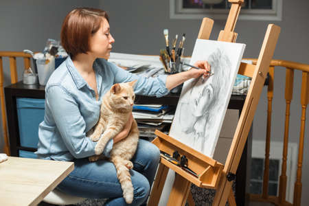 Concentrated middle age Caucasian woman artist drawing with pencil on canvas at home art studio....