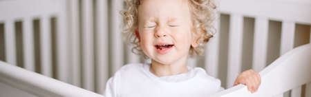 Kid tantrum. Baby boy crying in crib at kids nursery room at home. Funny baby boy with curly blond...