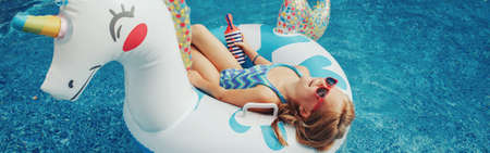 Girl in sunglasses with drink lying on inflatable ring unicorn. Kid child enjoying having fun...