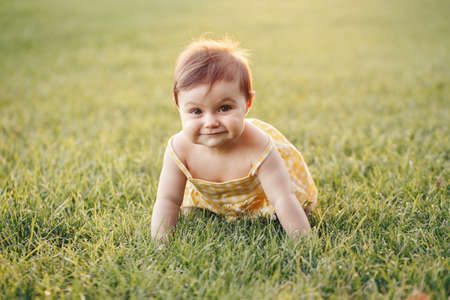Cute baby girl crawling on ground in park outdoors. Adorable child toddler exploring studying the world around. Healthy physical development. Funny kid. Authentic lifestyle happy childhood.の写真素材