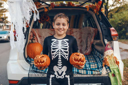 Trick or trunk. Boy child with red carved pumpkins celebrating Halloween in trunk of car. Happy kid...