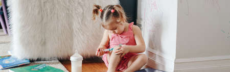 Funny cute baby girl drawing with marker on body legs. Toddler girl child playing at home. Authentic...