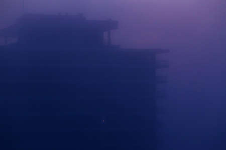 Smog fog in city at sunrise or night. Large apartment building with one lit window at night....