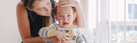 Mother hugging pacifying sad upset crying toddler boy. Family young mom and crying baby sitting on...
