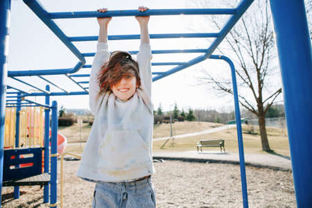Happy Caucasian girl hanging on monkey bars in park on playground. Summer outdoors activity for kids. Active preschool child doing exercises sport. Healthy happy authentic childhood.の写真素材