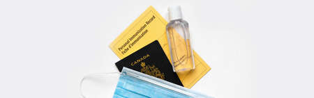 Vaccine passport for travel. Canadian passport with yellow immunity vaccination record in English and French languages, face mask and sanitizer. Safety measures against virus spread. Web banner headerの写真素材