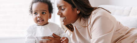 Happy smiling young Indian mother playing with black baby girl daughter. Family mixed race people mom and kid together. Authentic candid lifestyle with infant kid or child. Web banner header.の写真素材