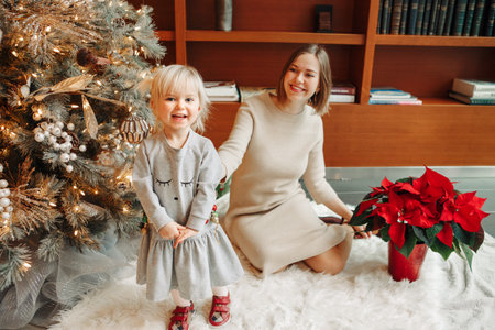Happy Caucasian mother with baby girl decorating Christmas tree with ornaments baubles toy. Happy family celebrating Christmas or New Year winter holiday at home. Winter holidays mood spiritの写真素材