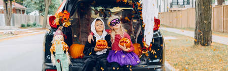Trick or trunk. Children celebrating Halloween in trunk of car. Boy and girl with red pumpkins celebrating traditional October holiday outdoors. Safe alternative celebration. Web banner header.の写真素材
