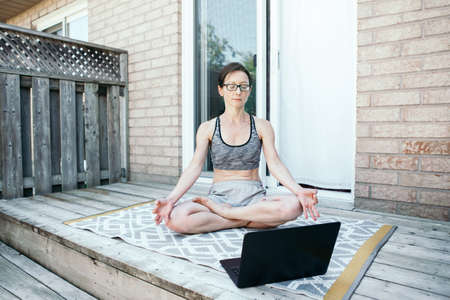 Middle age Caucasian woman practising yoga on backyard online. Video sport workout on Internet....