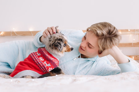 Young Caucasian woman with short hair lying on bed with cute puppy dog at home. Pet owner petting stroking little furry friend. Relationship of domestic animal and human.の写真素材