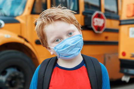 Boy kid student in protective face mask near school yellow bus outdoors. New normal at virus pandemic. Measurements against virus spread in class.の写真素材