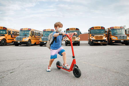 Boy in face protective mask riding scooter on school yard. Education and back to school in...