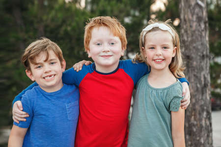 Three happy Caucasian little children kids boys and girl hugging together outdoor in park. Group of...