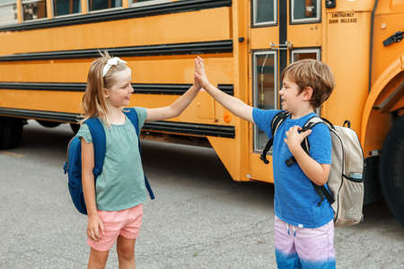 Children boy and girl kids students give hands high five by yellow school bus. Education and back to school in September. Friends schoolmates classmates meeting and greeting after summer break.の写真素材