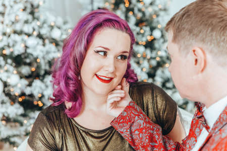 LGBTQ lesbian couple celebrating Christmas or New Year winter holiday together. Gay female lady with butch partner hugging cuddling on couch sofa at home. Winter holiday mood spirit. Couple in love.の写真素材