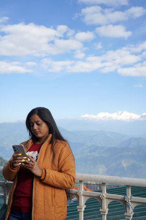 Young woman using smartphone while standing against a scenic Himalayan mountain backdrop