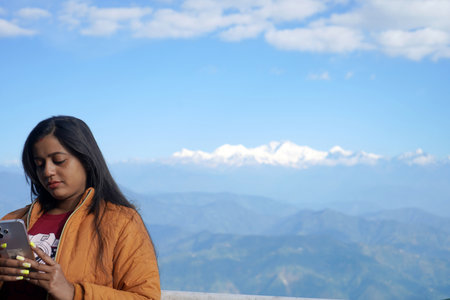 Indian woman in winter jacket using phone against Himalayan mountain range backgroundの写真素材