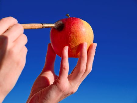 The artist holds an apple on a hand and paints it in red colorの写真素材
