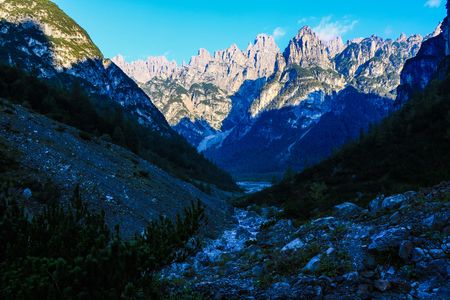 Narrow Alpine Valley with Mountains Peaks in the Background and a Flowing Creek - Postegae Valley - Friulane Dolomites Natural Park - Italyの写真素材