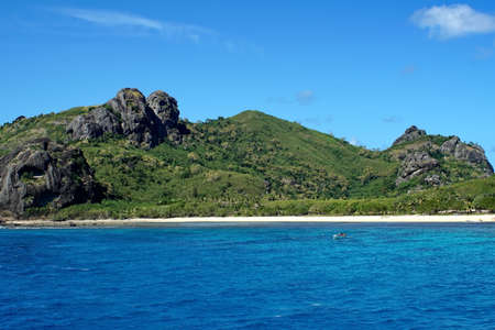 Clear blue water around a beach on a rugged island in Fijiの写真素材