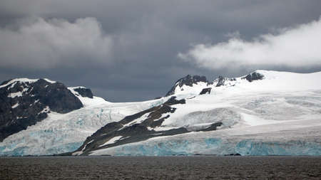 Rugged, snow covered mountains above a glacier in Antarcticaの写真素材