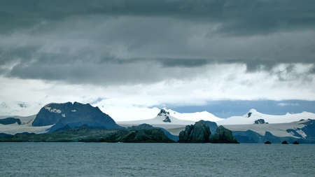Rugged coastline in front of a snow covered slope in Antarcticaの写真素材