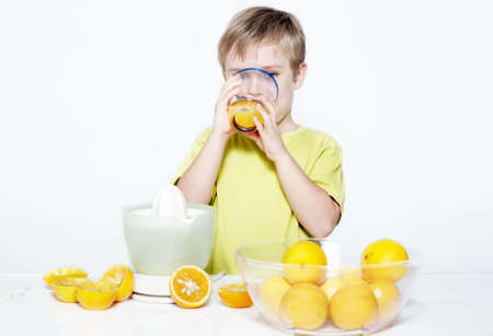 The boy drinking orange juice on a light backgroundの写真素材