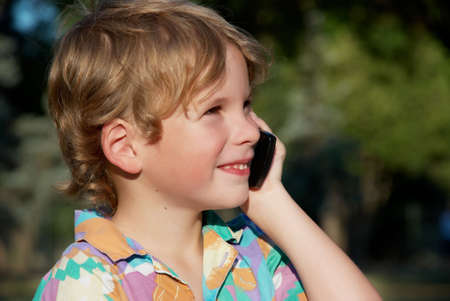 The cheerful boy with a mobile phone in parkの写真素材