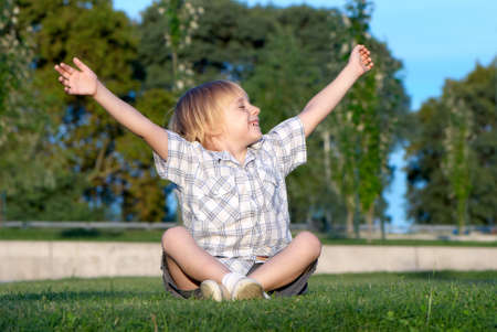 The little boy sitting on a grass with the lifted handsの写真素材