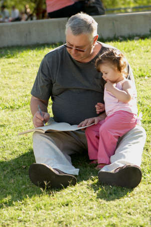 The grandfather with grand daughter sitting on a grass in parkの写真素材