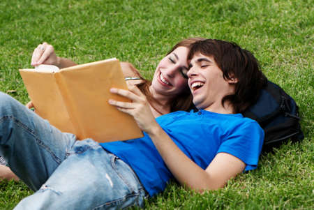 Couple students laying on the grass and reading a bookの写真素材