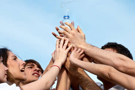 Group of young men stretching hands to a bottle with waterの写真素材