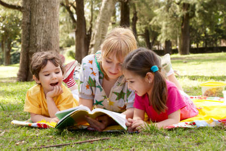  Elder sister reads to children of the book on a glade in park
の写真素材