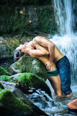 Couple hugging and kissing under waterfallの写真素材