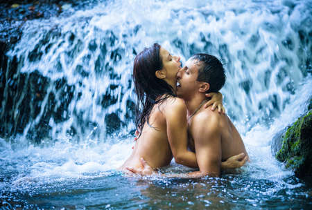 Couple hugging and kissing under waterfallの写真素材