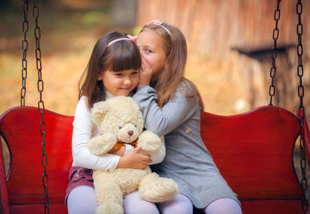 Happy little girlfriends on swing in parkの写真素材