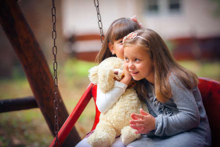 Happy little girlfriends on swing in parkの写真素材