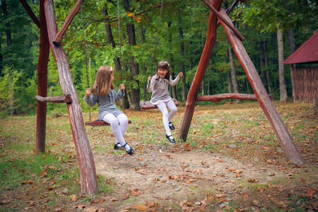 Happy little girlfriends on swing in parkの写真素材