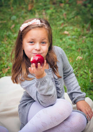 little girl is eating apple outdoorの写真素材
