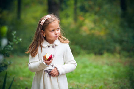 little girl is eating apple outdoorの写真素材